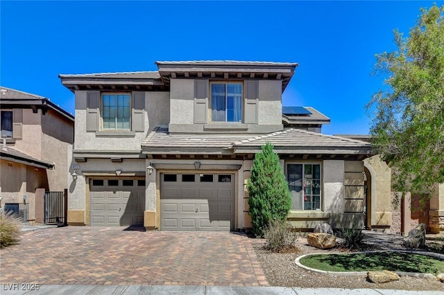 prairie-style house featuring roof mounted solar panels, decorative driveway, an attached garage, and stucco siding