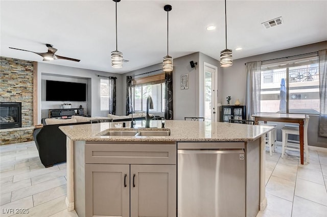 kitchen featuring a sink, stainless steel dishwasher, an island with sink, light tile patterned floors, and light stone counters