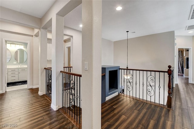 corridor with wood finished floors, an upstairs landing, baseboards, recessed lighting, and a chandelier