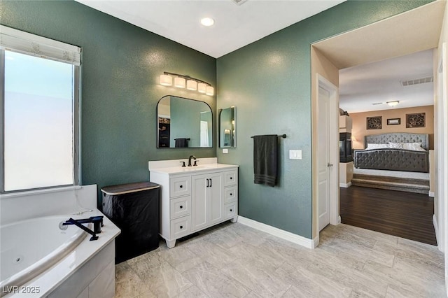 bathroom with ensuite bath, a textured wall, a tub with jets, baseboards, and vanity