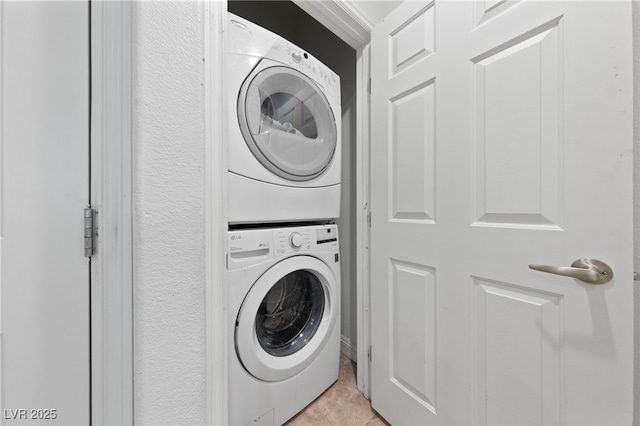 laundry area with stacked washer / drying machine, light tile patterned floors, and laundry area