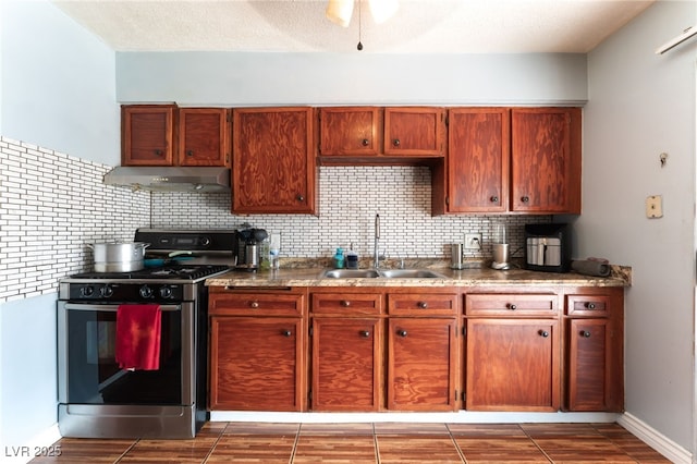 kitchen featuring stainless steel gas range oven, under cabinet range hood, a sink, tasteful backsplash, and baseboards