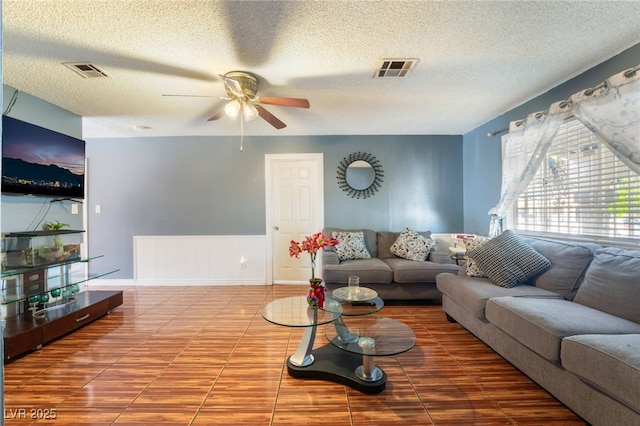tiled living area featuring a ceiling fan, a textured ceiling, and a wainscoted wall