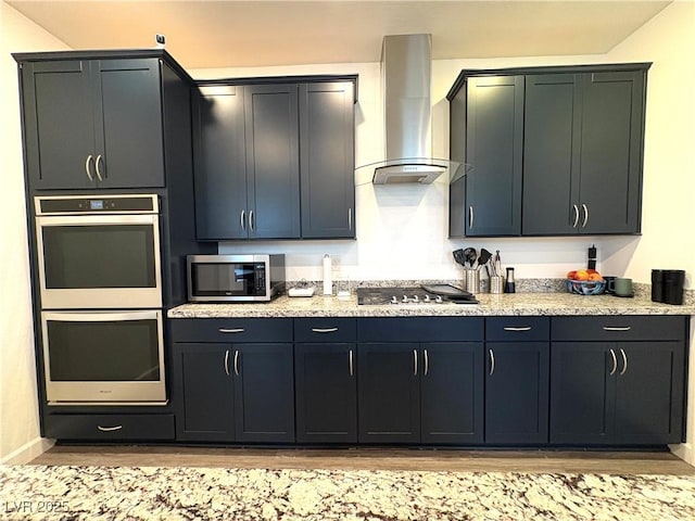 kitchen with appliances with stainless steel finishes, wall chimney exhaust hood, light wood-style floors, light stone counters, and baseboards