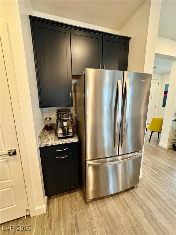 kitchen with freestanding refrigerator, light wood finished floors, baseboards, and dark cabinets