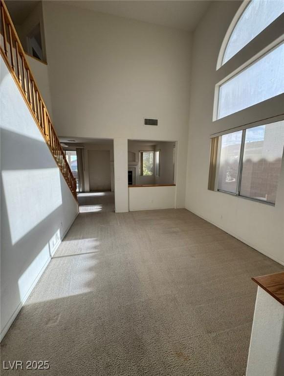 unfurnished living room featuring carpet floors, visible vents, stairs, and a high ceiling