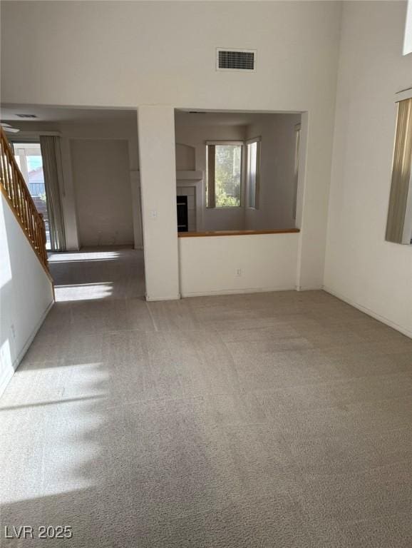 unfurnished living room with carpet flooring, visible vents, stairway, and a tiled fireplace