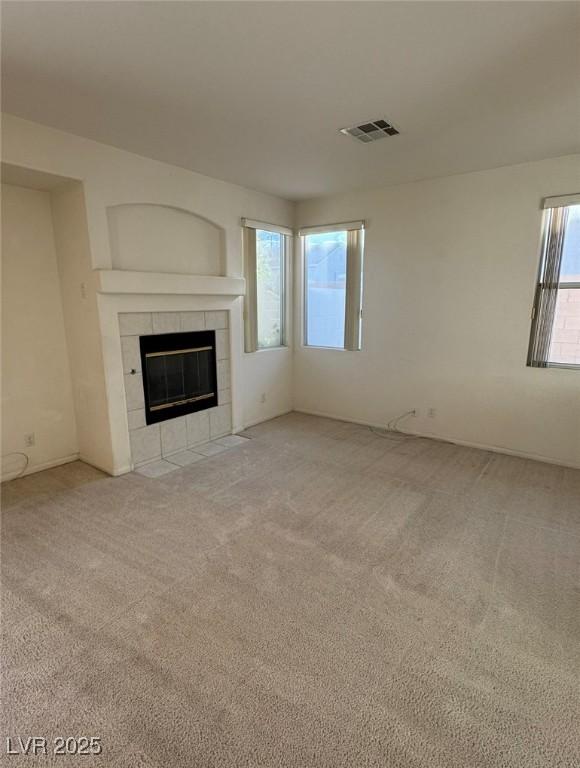 unfurnished living room featuring a tiled fireplace, visible vents, and carpet flooring