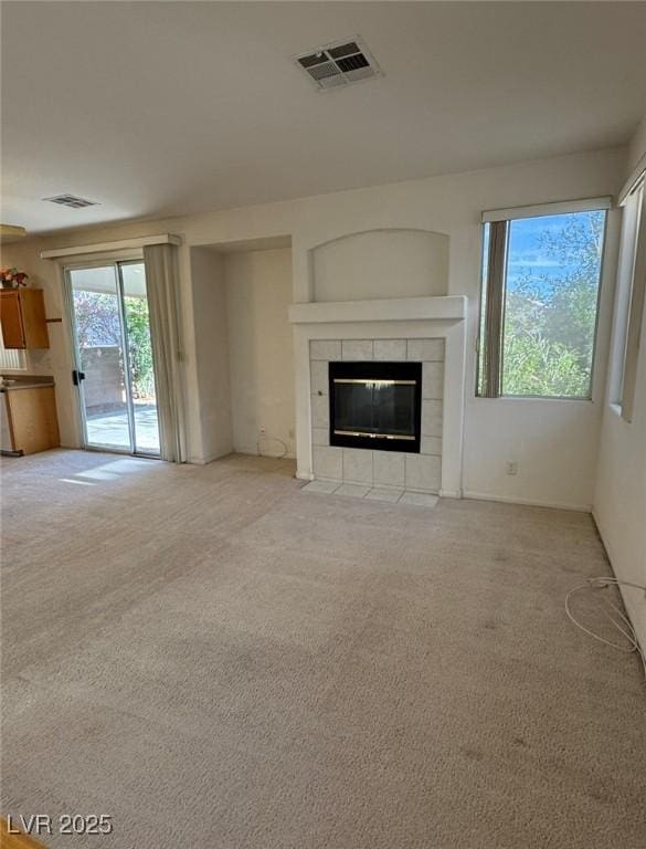 unfurnished living room with visible vents, a tile fireplace, and light colored carpet