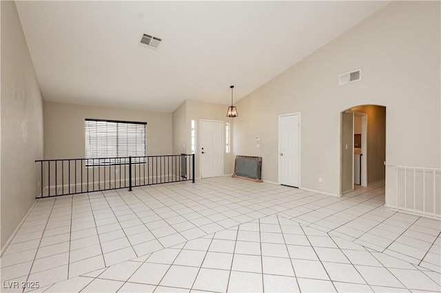 empty room with arched walkways, high vaulted ceiling, visible vents, and light tile patterned flooring