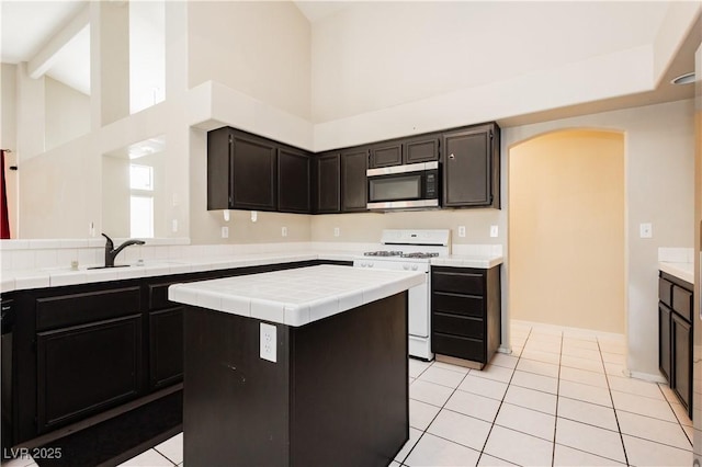 kitchen featuring arched walkways, a sink, high vaulted ceiling, white gas range oven, and stainless steel microwave