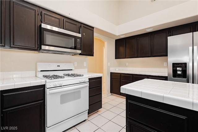 kitchen with stainless steel appliances, tile counters, light tile patterned floors, and arched walkways