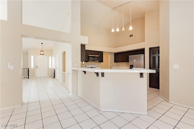 kitchen with a peninsula, appliances with stainless steel finishes, light tile patterned flooring, and a kitchen breakfast bar