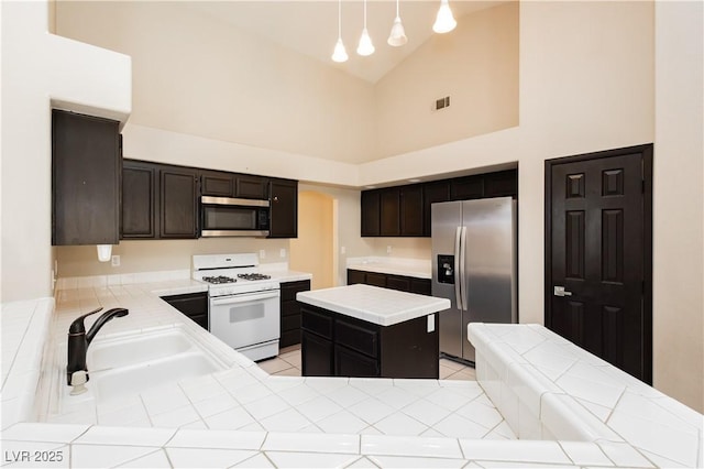 kitchen featuring appliances with stainless steel finishes, a sink, high vaulted ceiling, tile countertops, and visible vents