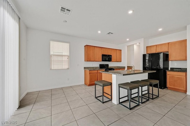 kitchen featuring recessed lighting, an island with sink, a kitchen breakfast bar, visible vents, and black appliances
