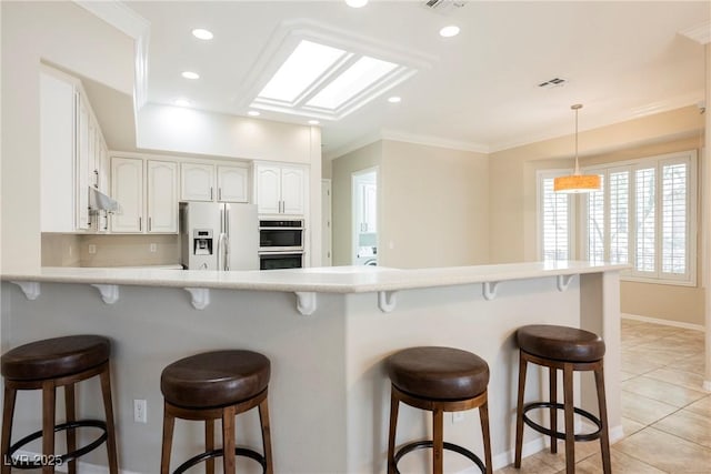 kitchen with stainless steel double oven, white refrigerator with ice dispenser, baseboards, visible vents, and a kitchen breakfast bar