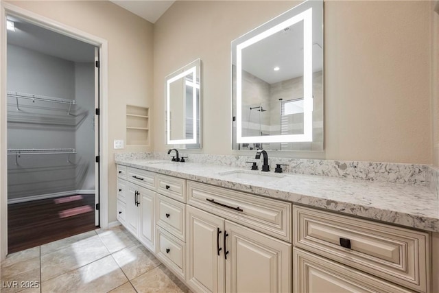 full bathroom featuring double vanity, a walk in closet, a shower stall, and a sink