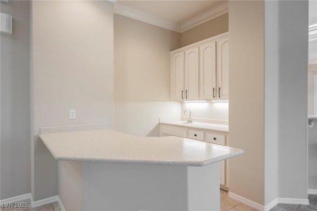 kitchen featuring white cabinets, a sink, light countertops, ornamental molding, and a peninsula
