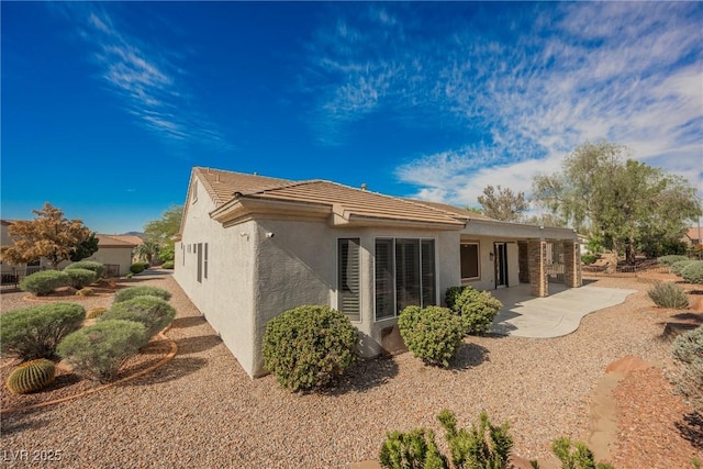 rear view of property with a tile roof, stucco siding, and a patio area