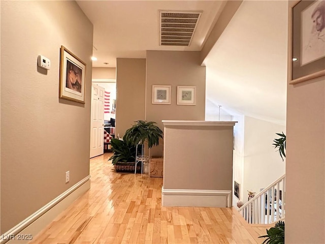 hall with baseboards, visible vents, an upstairs landing, and hardwood / wood-style floors