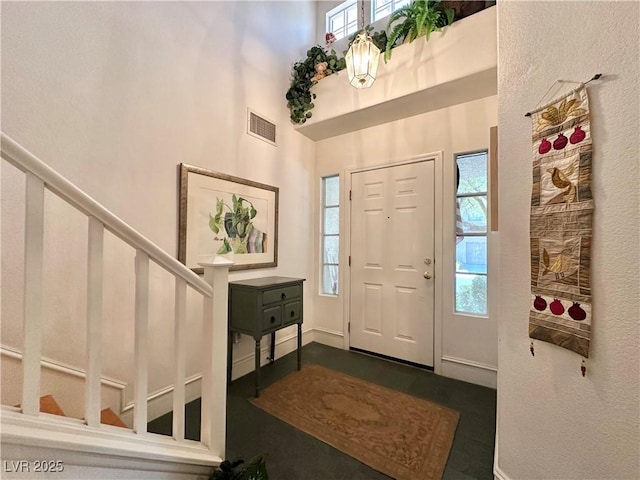 foyer entrance featuring a towering ceiling, visible vents, stairs, and a wealth of natural light