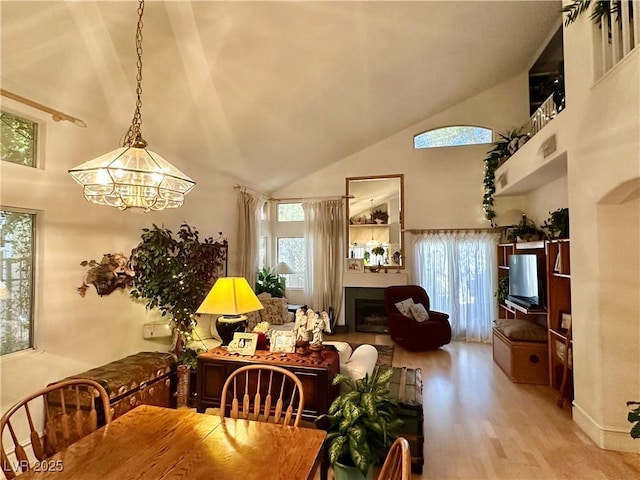dining room featuring high vaulted ceiling, a chandelier, wood finished floors, and a fireplace