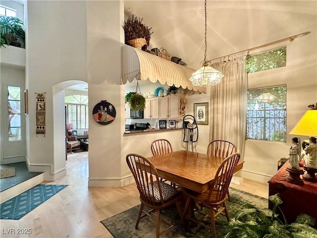 dining area with a towering ceiling, arched walkways, baseboards, a notable chandelier, and light wood-style flooring