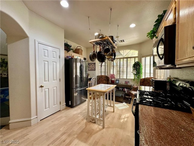 kitchen with dark countertops, light wood finished floors, arched walkways, a chandelier, and black appliances
