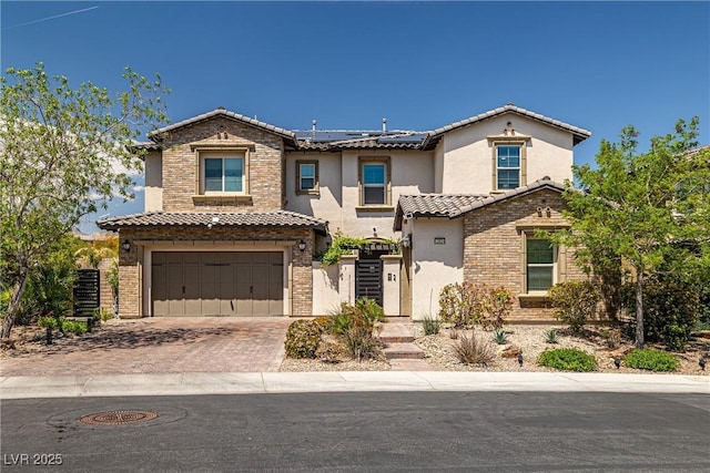 view of front of home with roof mounted solar panels, a tiled roof, decorative driveway, an attached garage, and stucco siding