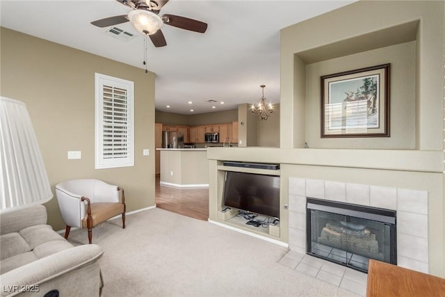 living room featuring light colored carpet, visible vents, baseboards, a fireplace, and ceiling fan with notable chandelier