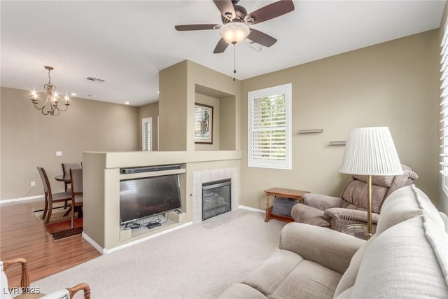 living area with a tile fireplace, visible vents, ceiling fan with notable chandelier, and baseboards
