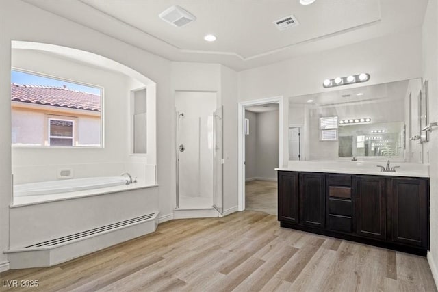 full bath with a baseboard heating unit, a shower stall, vanity, a garden tub, and wood finished floors