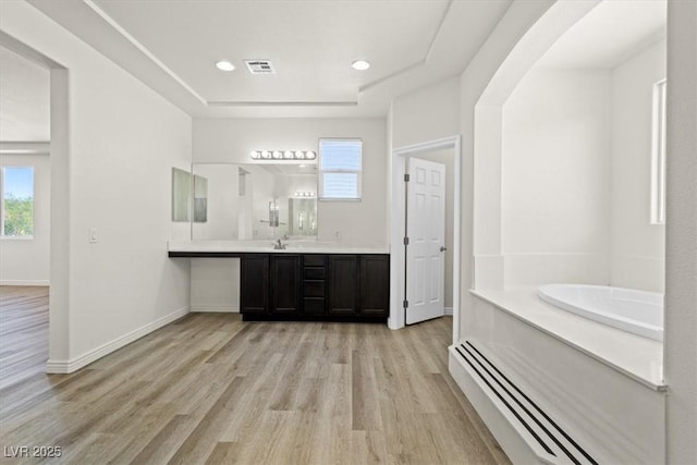 bathroom featuring visible vents, a tray ceiling, baseboard heating, a garden tub, and wood finished floors