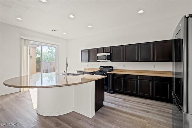 kitchen featuring stainless steel microwave, a sink, light wood-style floors, range with gas cooktop, and freestanding refrigerator