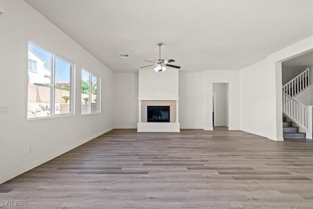 unfurnished living room featuring wood finished floors, stairs, ceiling fan, a glass covered fireplace, and baseboards