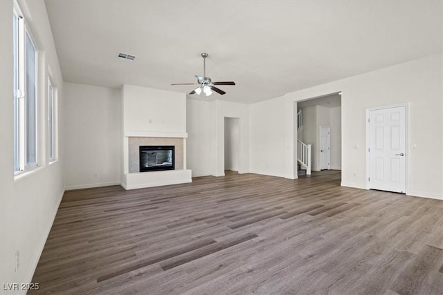 unfurnished living room featuring visible vents, ceiling fan, baseboards, a glass covered fireplace, and wood finished floors