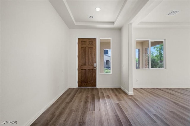 foyer featuring visible vents, baseboards, wood finished floors, and a tray ceiling