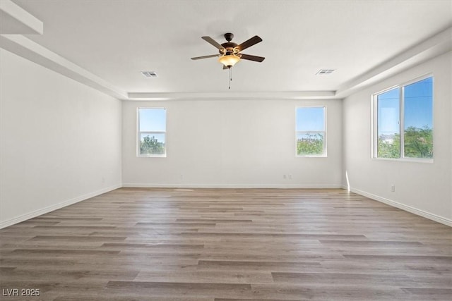 spare room with a ceiling fan, visible vents, wood finished floors, and baseboards