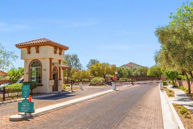 view of road featuring a gated entry, curbs, sidewalks, and traffic signs