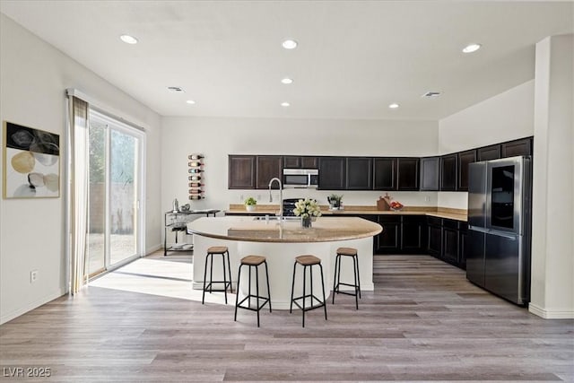 kitchen with recessed lighting, stainless steel appliances, a kitchen bar, and light wood-style flooring