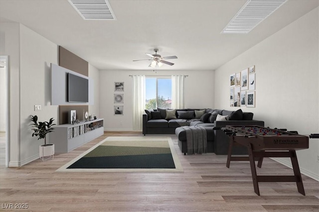 living room featuring a ceiling fan, visible vents, baseboards, and light wood-type flooring