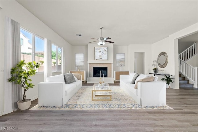 living room featuring a ceiling fan, stairway, wood finished floors, and a glass covered fireplace