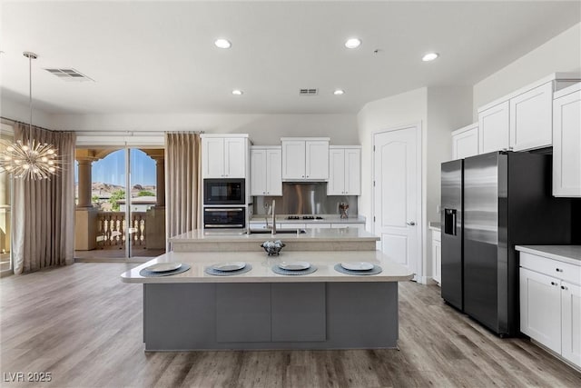kitchen with black microwave, visible vents, stainless steel refrigerator with ice dispenser, light countertops, and wall oven