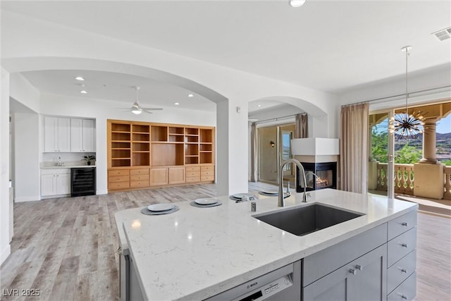 kitchen featuring beverage cooler, light stone counters, a multi sided fireplace, a sink, and open floor plan
