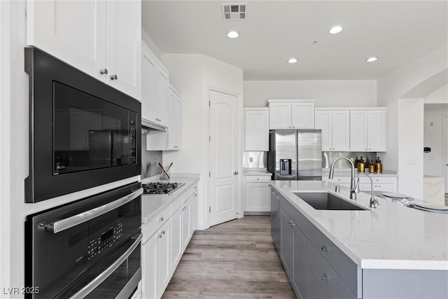 kitchen with stainless steel appliances, white cabinets, light wood finished floors, a sink, and visible vents