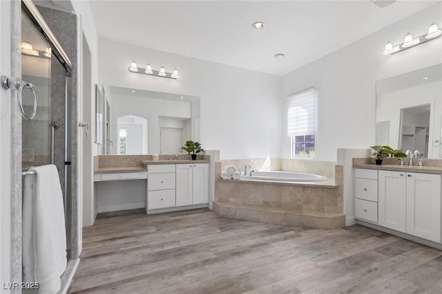 full bathroom featuring wood finished floors, two vanities, a stall shower, and a bath