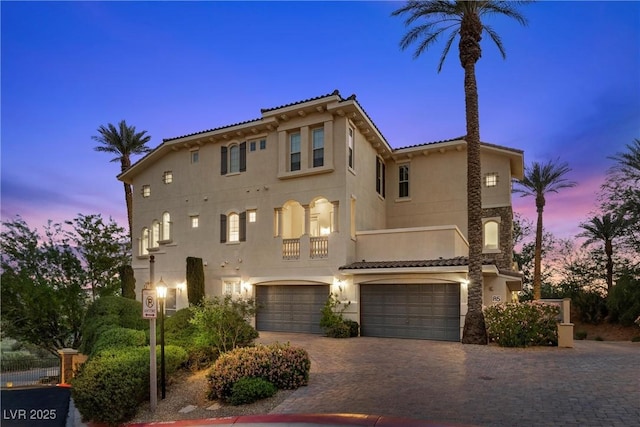 mediterranean / spanish house featuring an attached garage, a tile roof, and stucco siding