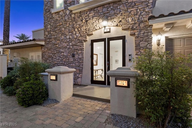 exterior entry at dusk featuring stucco siding and stone siding
