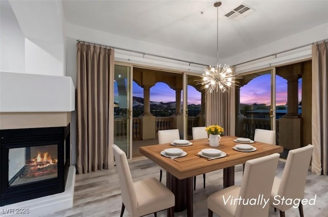 dining room with visible vents, wood finished floors, an inviting chandelier, and a multi sided fireplace