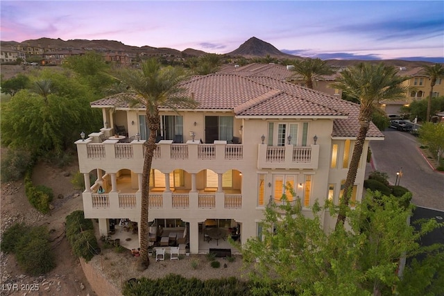 back of property featuring stucco siding, a tiled roof, a balcony, and a mountain view